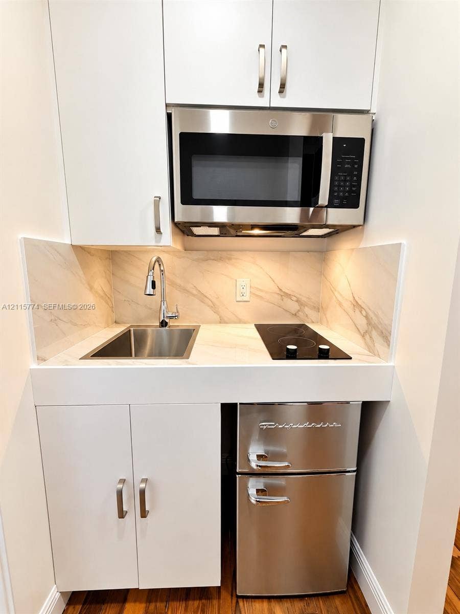 1455 Michigan Avenue, #19A, Miami Beach, Miami Beach, FL 33139 Compact kitchenette featuring white cabinetry, stone-finish backsplash and countertop, stainless steel sink with pull-down faucet, glass cooktop, and over-the-range microwave