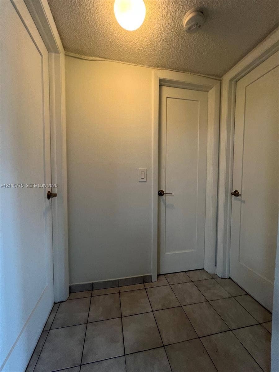 479 E 13th Street, #479, Hialeah, Hialeah, FL 33010 Interior space featuring square ceramic tile flooring, three solid-core shaker-style doors with metallic hardware, and a flush-mount ceiling light fixture