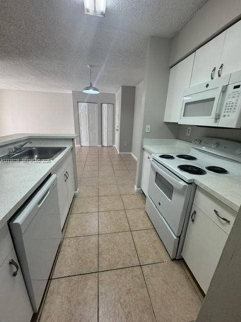 Kitchen featuring white cabinetry, solid-surface countertops, tile flooring, and built-in appliances including a dishwasher, range, and microwave