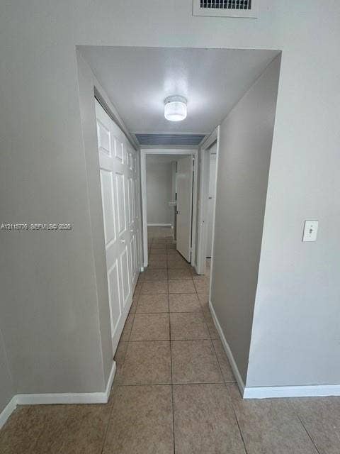 Hallway featuring neutral-toned tile flooring, recessed-panel closet doors, and a flush-mount ceiling light fixture