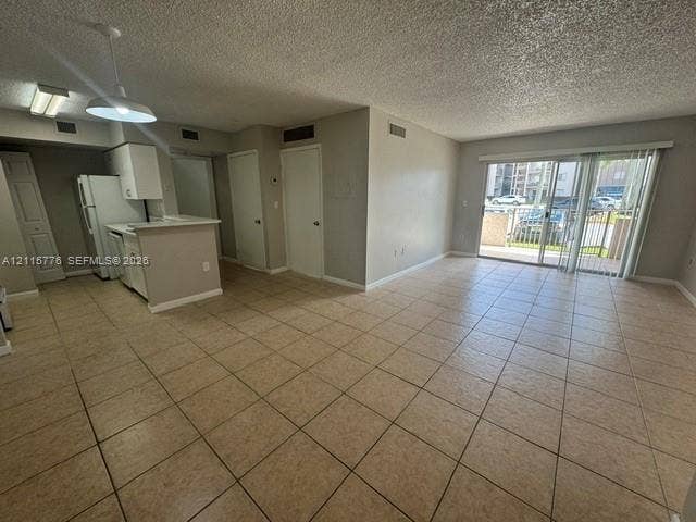 Open-concept main living area featuring ceramic tile flooring, kitchen with peninsula, and large glass sliding doors providing exterior access