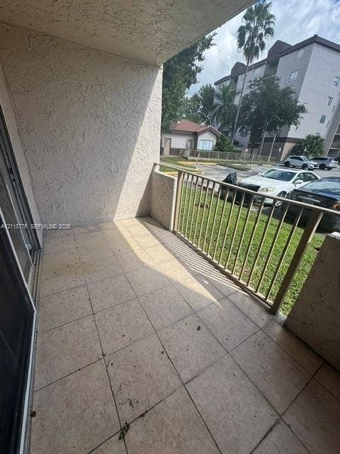 Covered balcony featuring concrete tile flooring, stucco wall finish, and metal railing