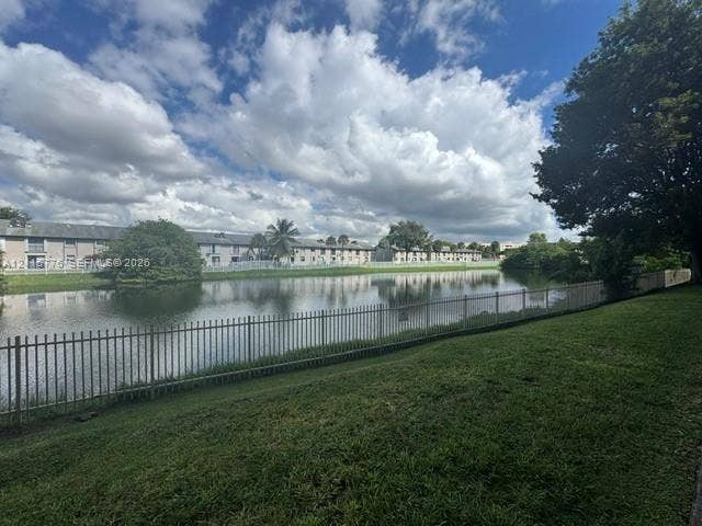 Waterfront lot featuring a manicured lawn, perimeter metal fencing, and mature trees