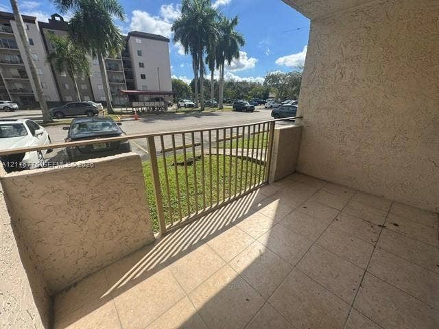 Covered patio featuring ceramic tile flooring, a textured stucco exterior wall, and a metal railing
