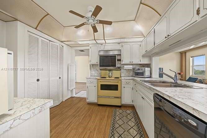 215 SE 3rd Avenue, #501B, Hallandale Beach, FL 33009 Kitchen featuring white cabinetry, wood-finish flooring, stone-patterned countertops, a stainless steel double-basin sink, and a tray ceiling with a central ceiling fan