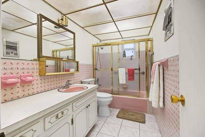 215 SE 3rd Avenue, #501B, Hallandale Beach, FL 33009 Bathroom featuring a built-in vanity with countertop sink, patterned tile wall accents, a bathtub with sliding glass doors, and a decorative grid ceiling