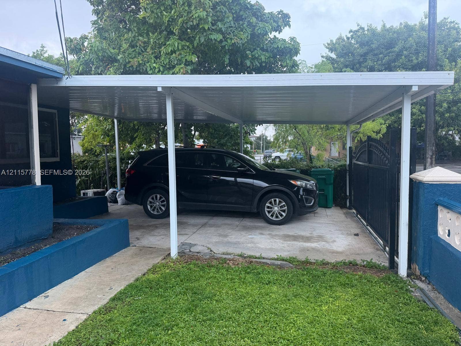 Covered carport with concrete flooring, secure metal gate, and masonry perimeter wall