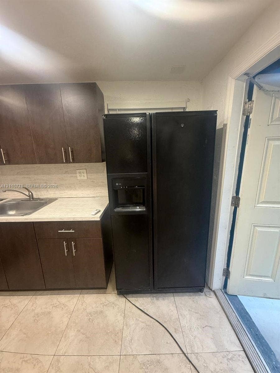 Kitchen featuring dark wood-finish cabinetry, stone-finish countertops, stainless steel sink with metal faucet, and black side-by-side refrigerator