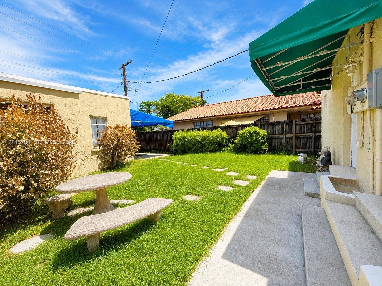 3655 SW 24th Terrace, #1, Miami, Miami, FL 33145 Exterior courtyard featuring a grass lawn, paved stone pathway, green retractable awning, and textured stucco walls