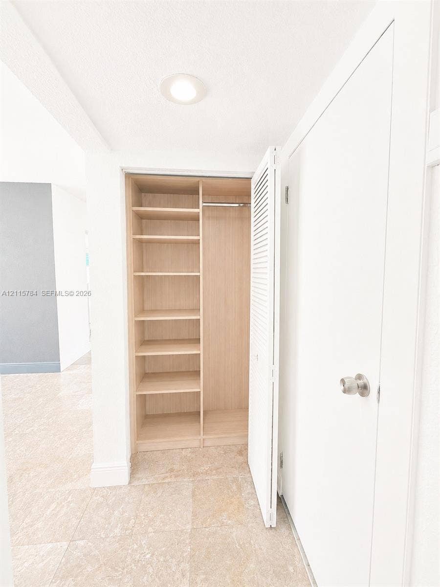3655 SW 24th Terrace, #1, Miami, Miami, FL 33145 Built-in closet featuring light-toned wood shelving, a metal garment rod, and louvered folding doors, set against stone-finish flooring and recessed ceiling lighting