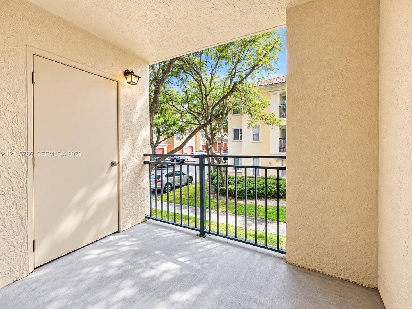 2494 Centergate Drive, #202, Miramar, Miramar, FL 33025 Covered balcony featuring textured exterior walls, concrete flooring, black metal railing, and an attached storage closet with exterior lighting