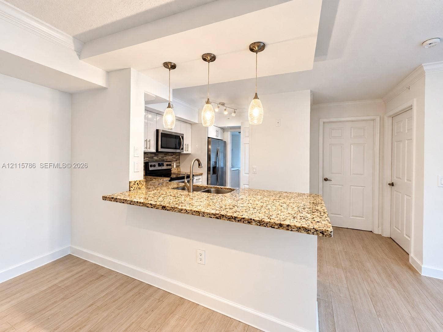 2494 Centergate Drive, #202, Miramar, Miramar, FL 33025 Kitchen featuring a stone-surface breakfast bar, wood-finish flooring, white shaker-style cabinetry, a stainless steel undermount sink, and three pendant light fixtures