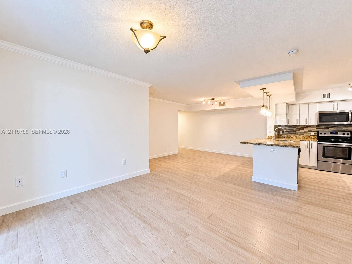 2494 Centergate Drive, #202, Miramar, Miramar, FL 33025 Open-concept interior featuring light wood-finish flooring, kitchen island with stone countertop, stainless steel appliances, tiled backsplash, and recessed and pendant lighting