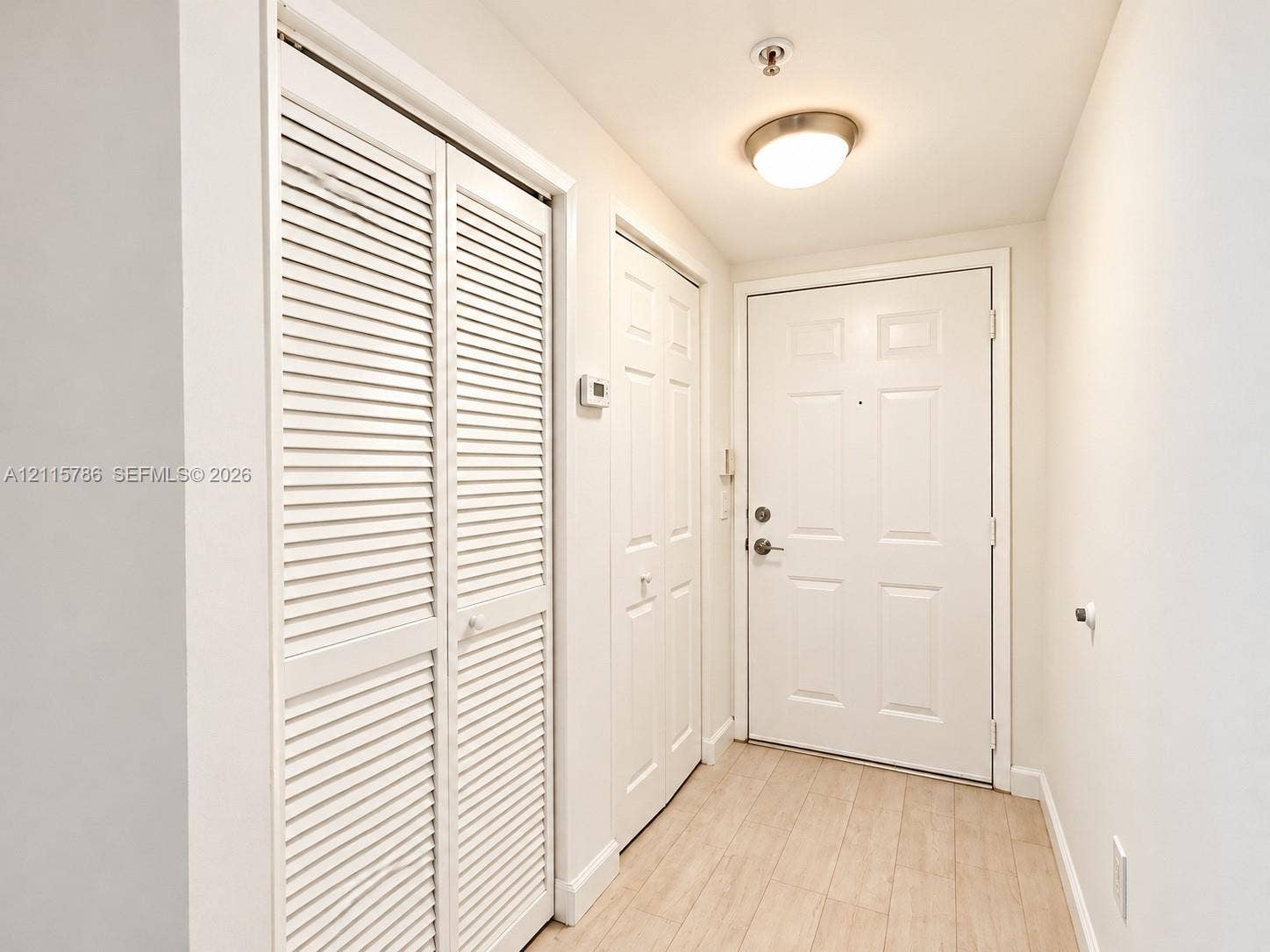 2494 Centergate Drive, #202, Miramar, Miramar, FL 33025 Entryway featuring light-toned wood-finish flooring, white louvered-style closet doors, a paneled solid entry door with integrated deadbolt, and a flush-mount dome light fixture