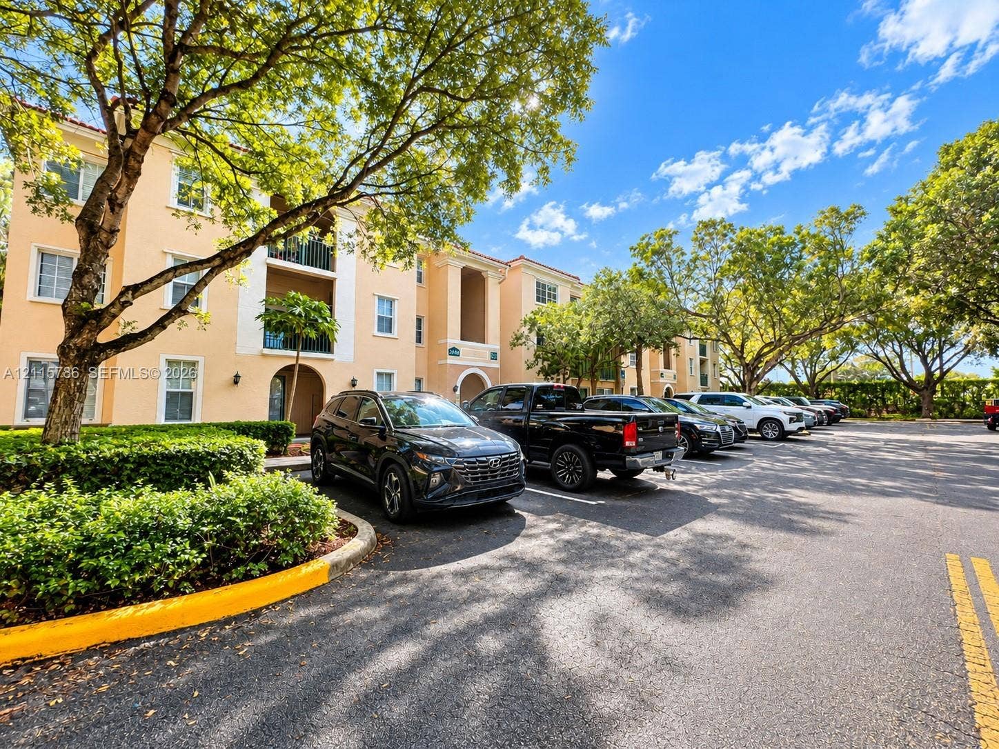 2494 Centergate Drive, #202, Miramar, Miramar, FL 33025 Stucco exterior building featuring balconies, tile roofing, and paved surface parking surrounded by mature landscaping