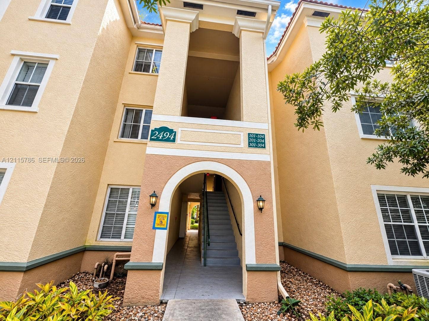 2494 Centergate Drive, #202, Miramar, Miramar, FL 33025 Stucco exterior featuring a prominent arched entry, tiered architectural facade, dual wall-mounted coach lights, and multi-pane windows