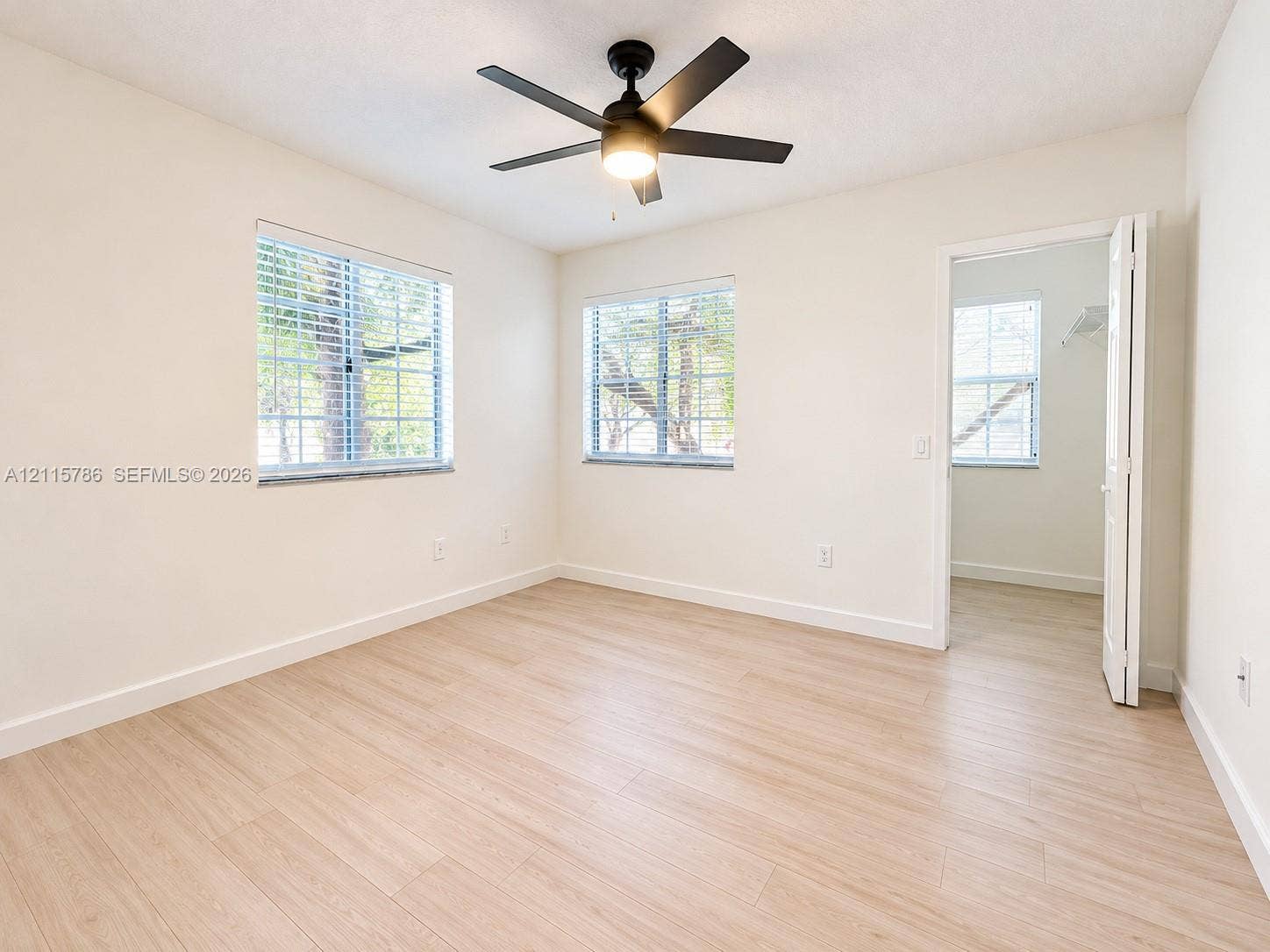 2494 Centergate Drive, #202, Miramar, Miramar, FL 33025 Neutral-toned wood-finish flooring, matte black ceiling fan with integrated lighting, and multiple windows with horizontal blinds