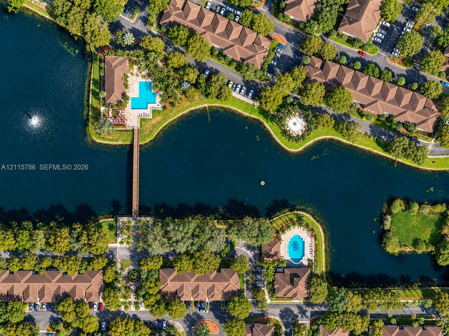 2494 Centergate Drive, #202, Miramar, Miramar, FL 33025 Aerial perspective of a community featuring a central waterway, pedestrian footbridge, swimming pools, and mature trees
