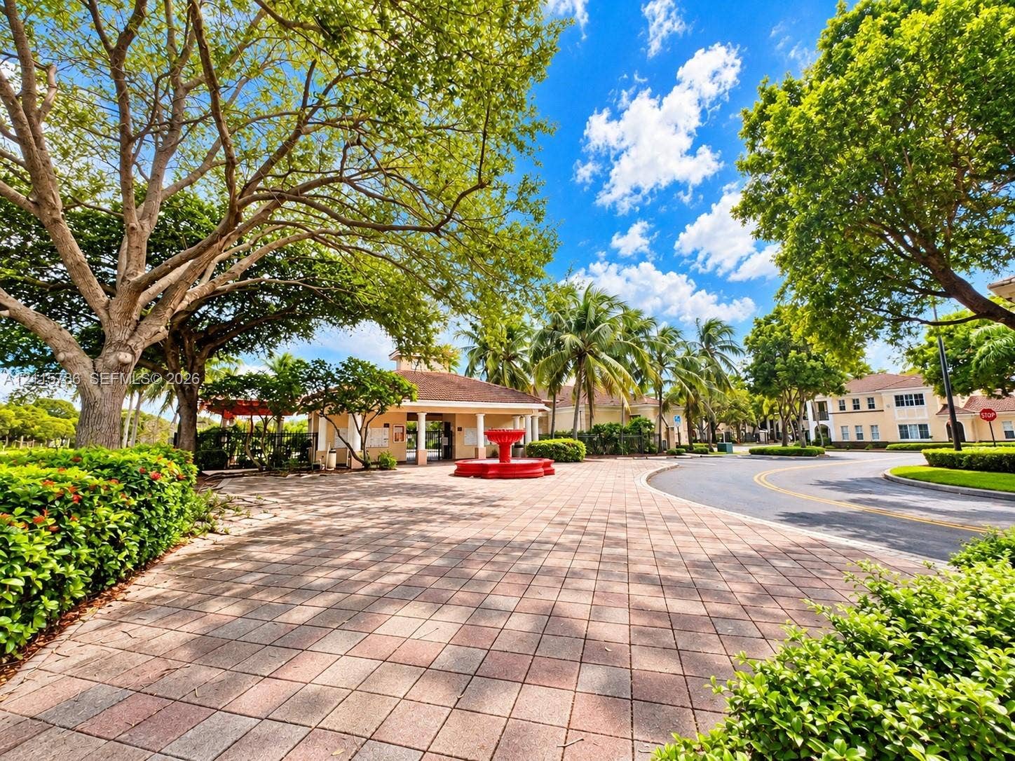 2494 Centergate Drive, #202, Miramar, Miramar, FL 33025 Paver stone entryway featuring a central fountain, mature canopy trees, manicured hedges, and a covered clubhouse structure