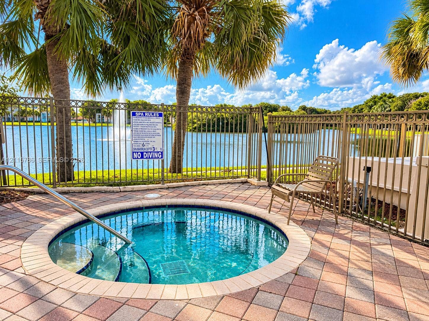 2494 Centergate Drive, #202, Miramar, Miramar, FL 33025 In-ground spa with stone paver surround, metal safety fencing, and palm-lined waterfront setting