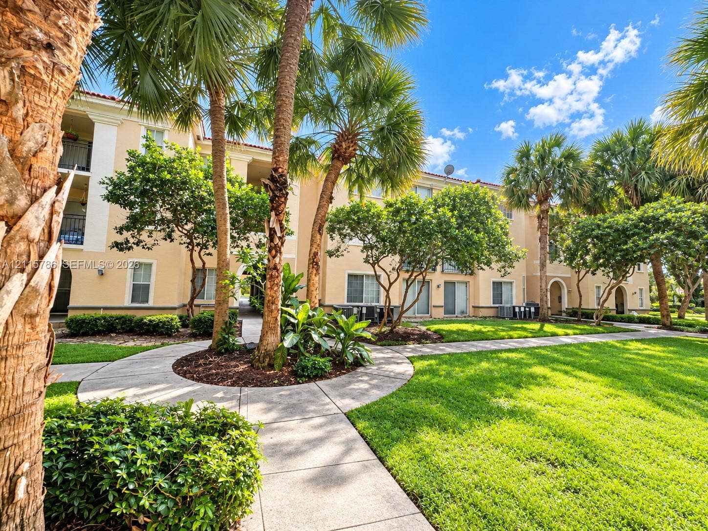 2494 Centergate Drive, #202, Miramar, Miramar, FL 33025 Stucco exterior featuring arched entryways and multi-level balconies, complemented by mature palm trees, professional landscaping, and concrete pathways