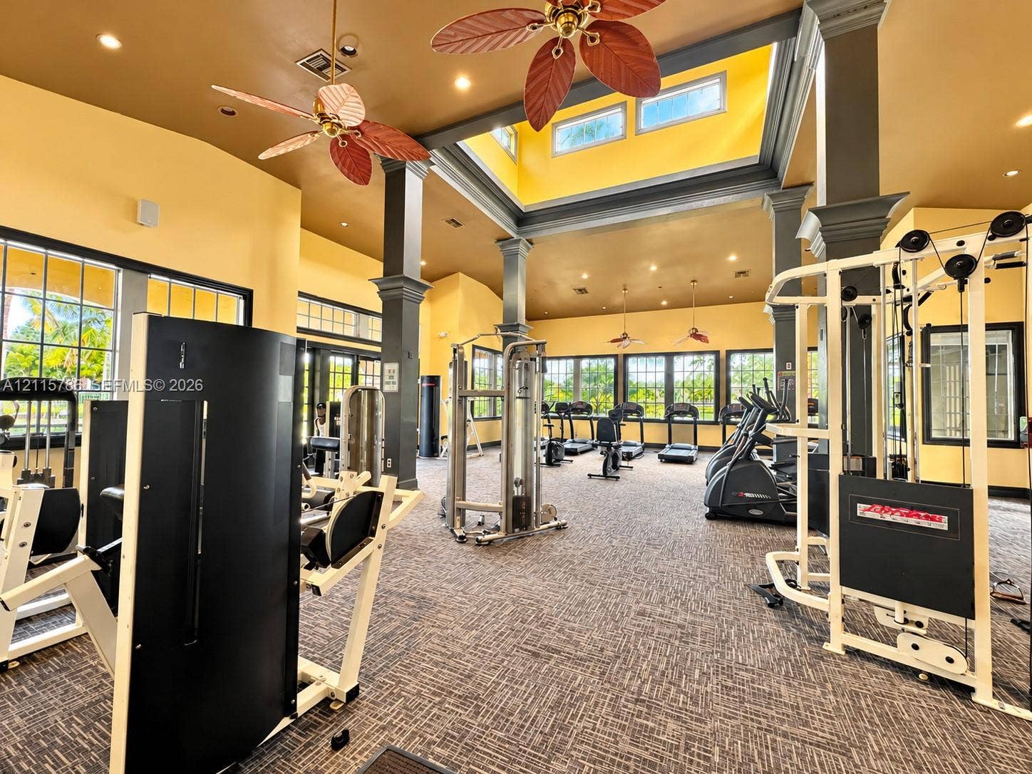 2494 Centergate Drive, #202, Miramar, Miramar, FL 33025 High-ceiling fitness space featuring a central skylight, structural columns with decorative trim, multiple large-pane windows, and inset recessed lighting