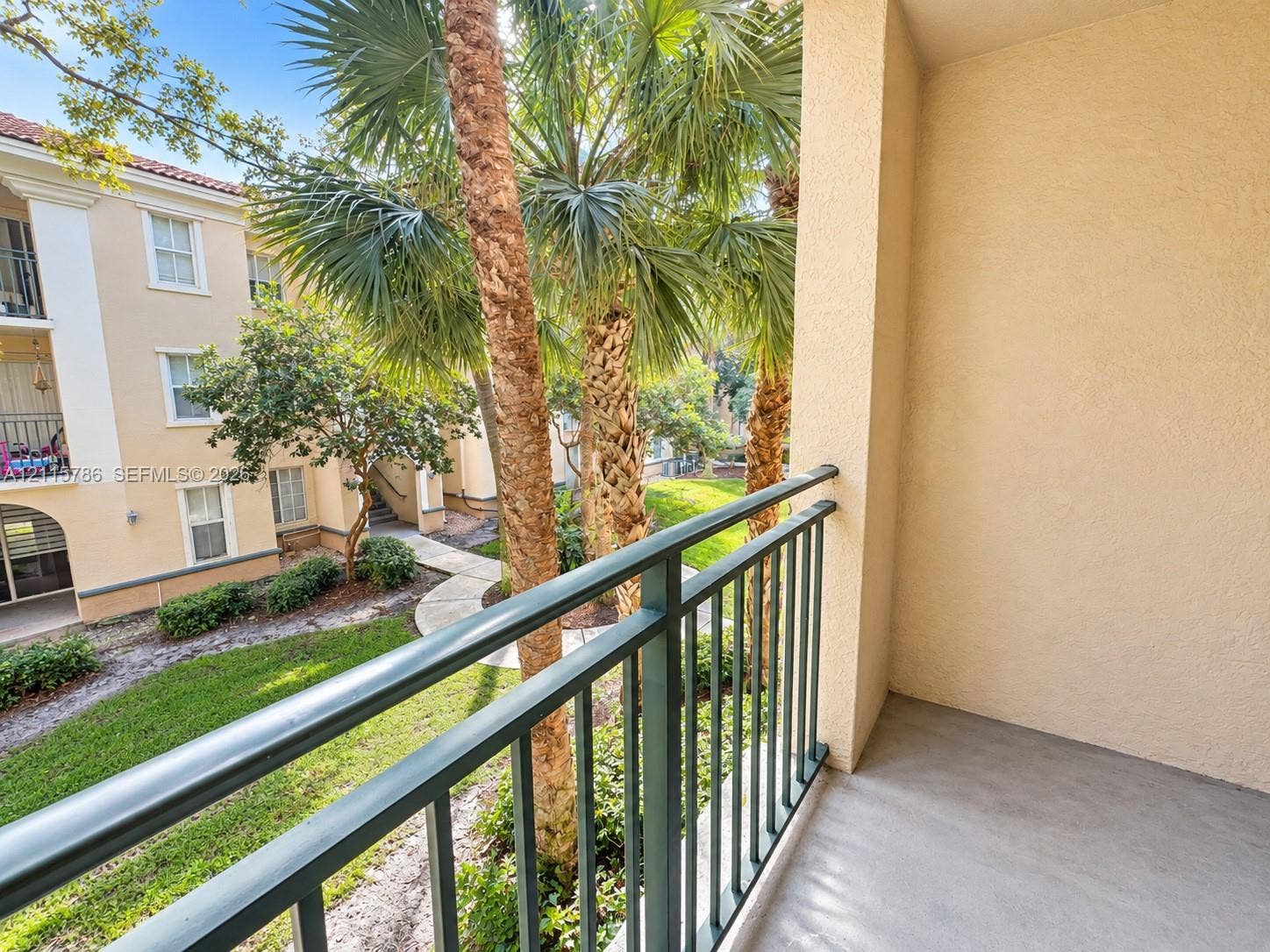 2494 Centergate Drive, #202, Miramar, Miramar, FL 33025 Private balcony featuring textured stucco walls, solid surface flooring, and metal railing overlooking landscaped grounds with mature palm trees
