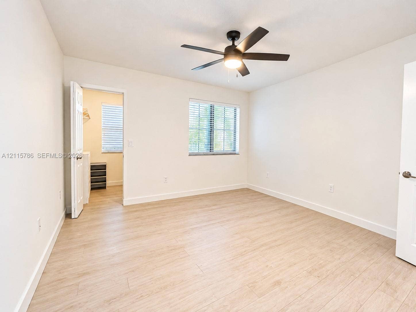 2494 Centergate Drive, #202, Miramar, Miramar, FL 33025 Neutral-toned interior space featuring wood-finish flooring, a ceiling fan with integrated lighting, and a multi-pane window