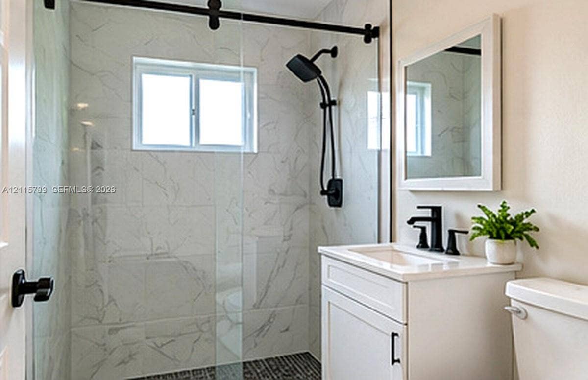 16220 NW 28th Place, Miami Gardens, FL 33054 Bathroom featuring a walk-in shower with stone-patterned wall tile, a frameless glass door with matte black hardware, a black rainfall showerhead, and a vanity with a white rectangular sink