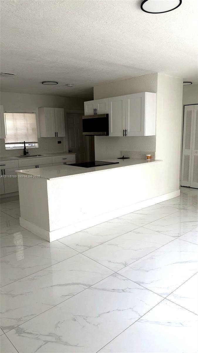 16220 NW 28th Place, Miami Gardens, FL 33054 Kitchen featuring white shaker-style cabinetry, quartz countertops, a peninsula with an integrated cooktop, and large-format porcelain tile flooring