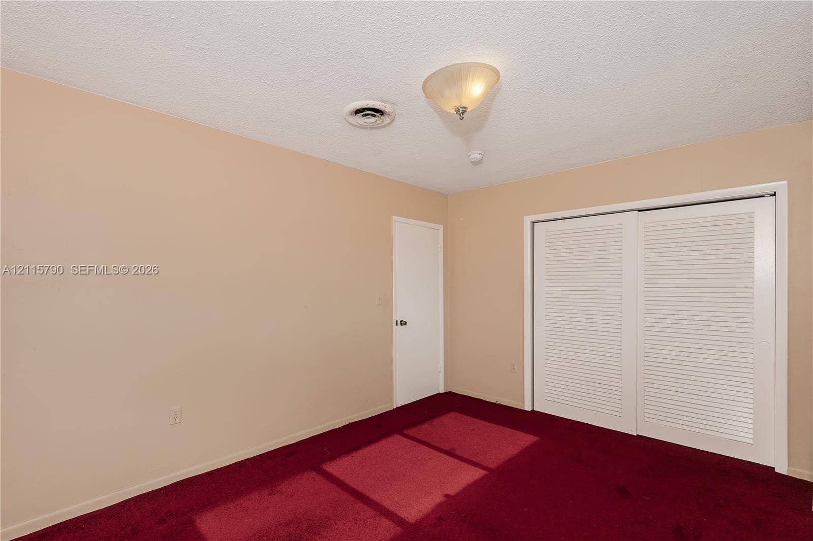 9120 NW 12th Avenue, Miami, FL 33150 Room featuring red wall-to-wall carpeting, dual-panel louvered closet doors, and a semi-flush mount ceiling light fixture