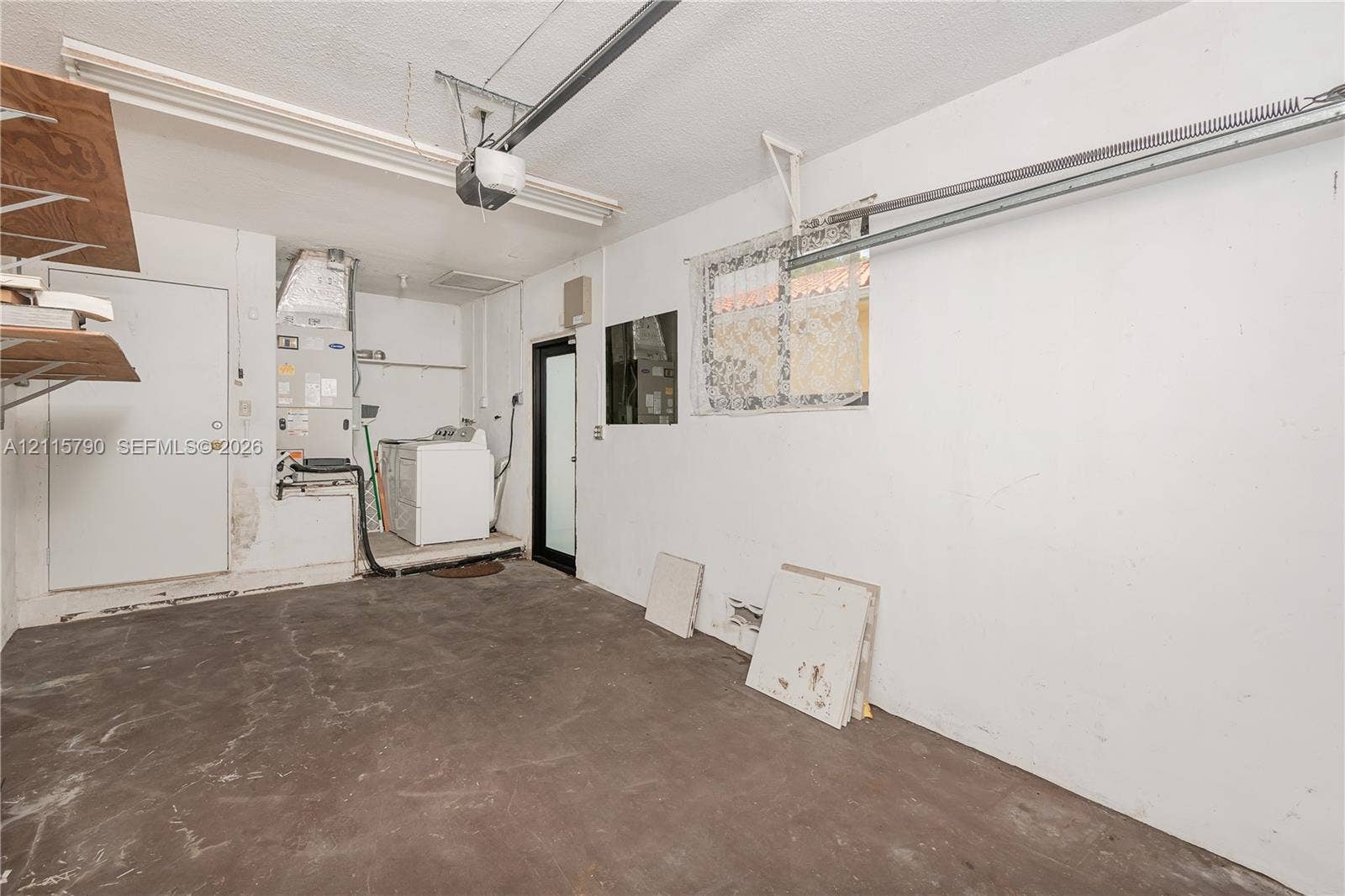 9120 NW 12th Avenue, Miami, FL 33150 Garage space featuring concrete flooring, an overhead door motor, built-in shelving, a dedicated laundry area, and a glass-paneled entry door