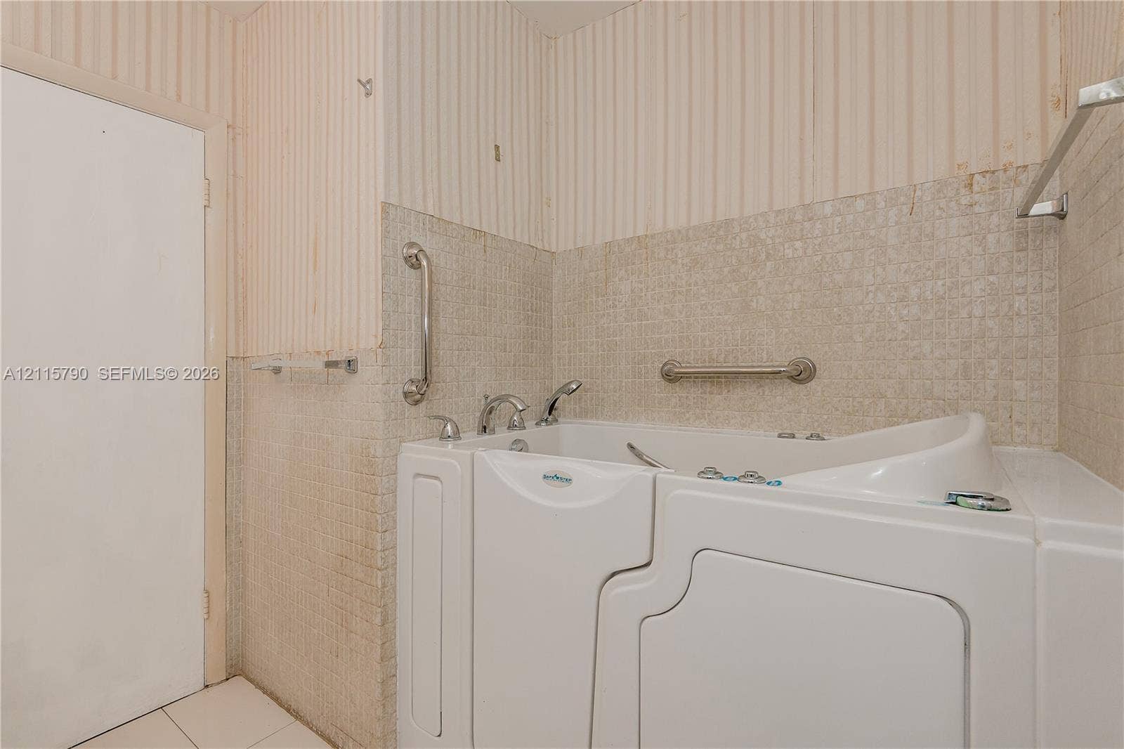 9120 NW 12th Avenue, Miami, FL 33150 Walk-in tub featuring a side-entry door, chrome faucet fixtures, and mounted safety grab bars, complemented by neutral square wall tiling