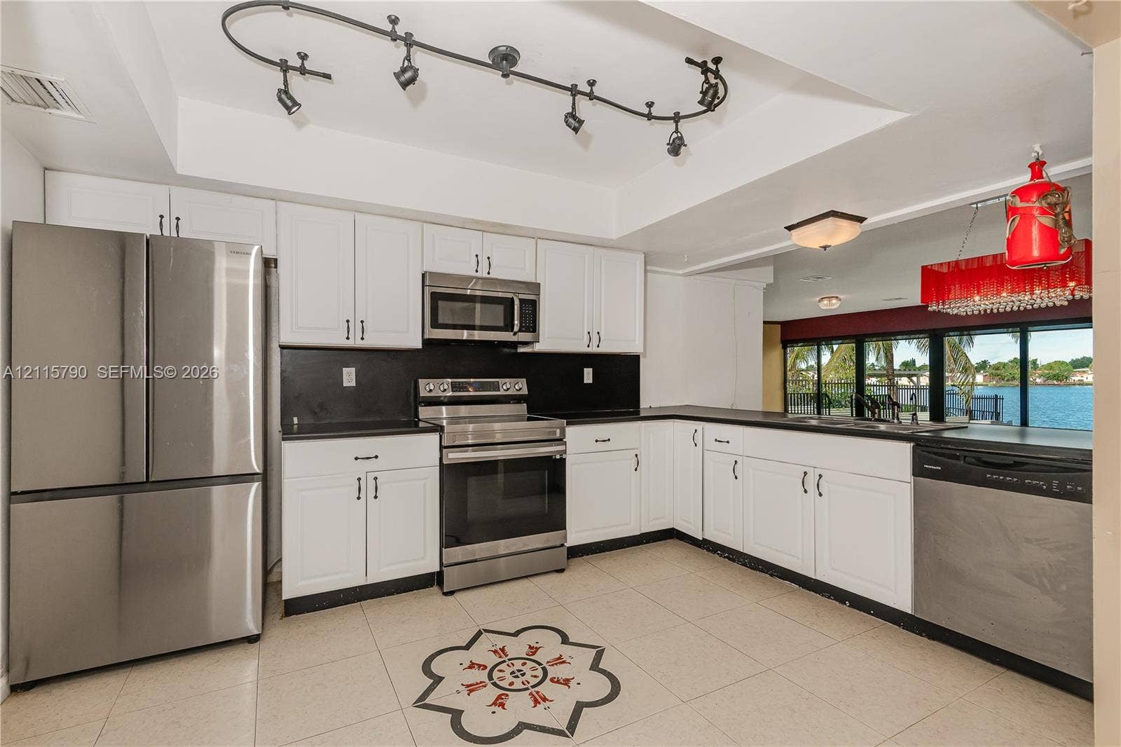 9120 NW 12th Avenue, Miami, FL 33150 Kitchen featuring white shaker-style cabinetry, black countertops, stainless steel appliances, tile flooring with a central decorative inlay, and adjustable track lighting
