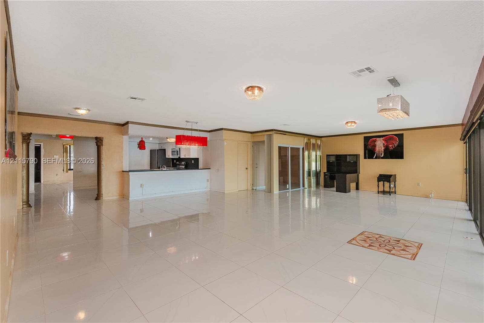 9120 NW 12th Avenue, Miami, FL 33150 Open-concept interior featuring large-format ceramic tile flooring, built-in breakfast bar with stone-finish countertop, decorative architectural columns, multiple hanging light fixtures, and sliding glass doors