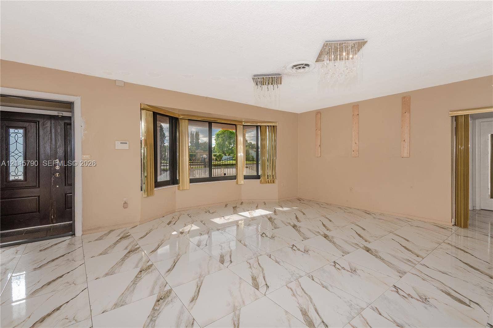9120 NW 12th Avenue, Miami, FL 33150 Large-format stone-style tile flooring, expansive bay window, ornate crystal-style ceiling light fixtures, and solid-core dark wood entry door with decorative glass inlay
