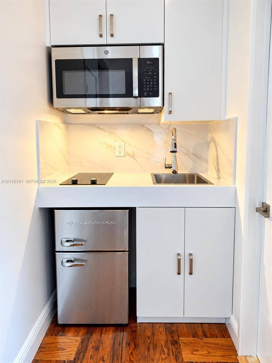 1455 Michigan Avenue, #19B, Miami Beach, Miami Beach, FL 33139 Kitchenette featuring white cabinetry with stainless steel pulls, a stone-patterned backsplash, stainless steel microwave, inset cooktop, and under-counter refrigeration unit
