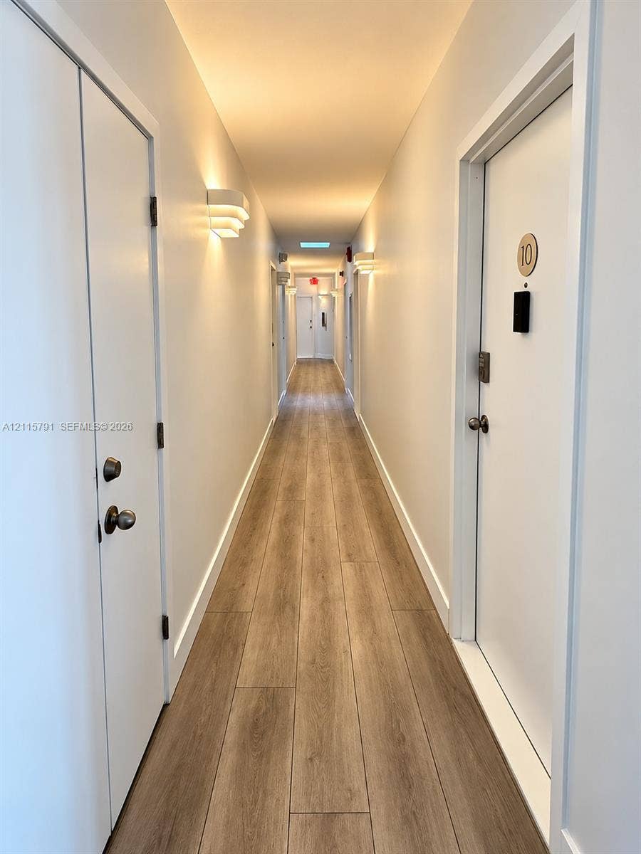 1455 Michigan Avenue, #19B, Miami Beach, Miami Beach, FL 33139 Hallway featuring wood-finish flooring, white doors with metallic hardware, and wall-mounted sconce lighting