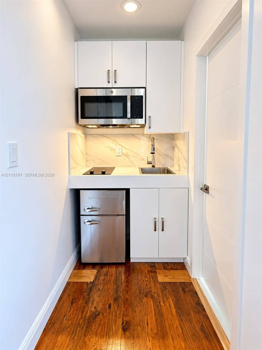 1455 Michigan Avenue, #19B, Miami Beach, Miami Beach, FL 33139 Kitchenette featuring white shaker cabinetry, stone-patterned backsplash, stainless steel microwave, inset electric cooktop, and wood-finish flooring