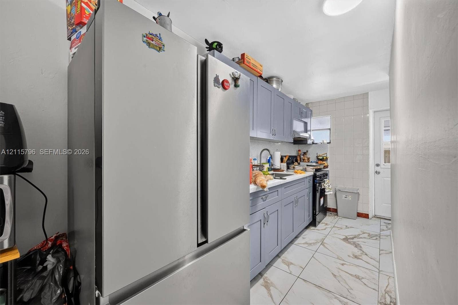 Kitchen featuring grey shaker-style cabinetry, stainless steel french-door refrigerator, tile backsplash, stone-finish floor tile, and exterior access door