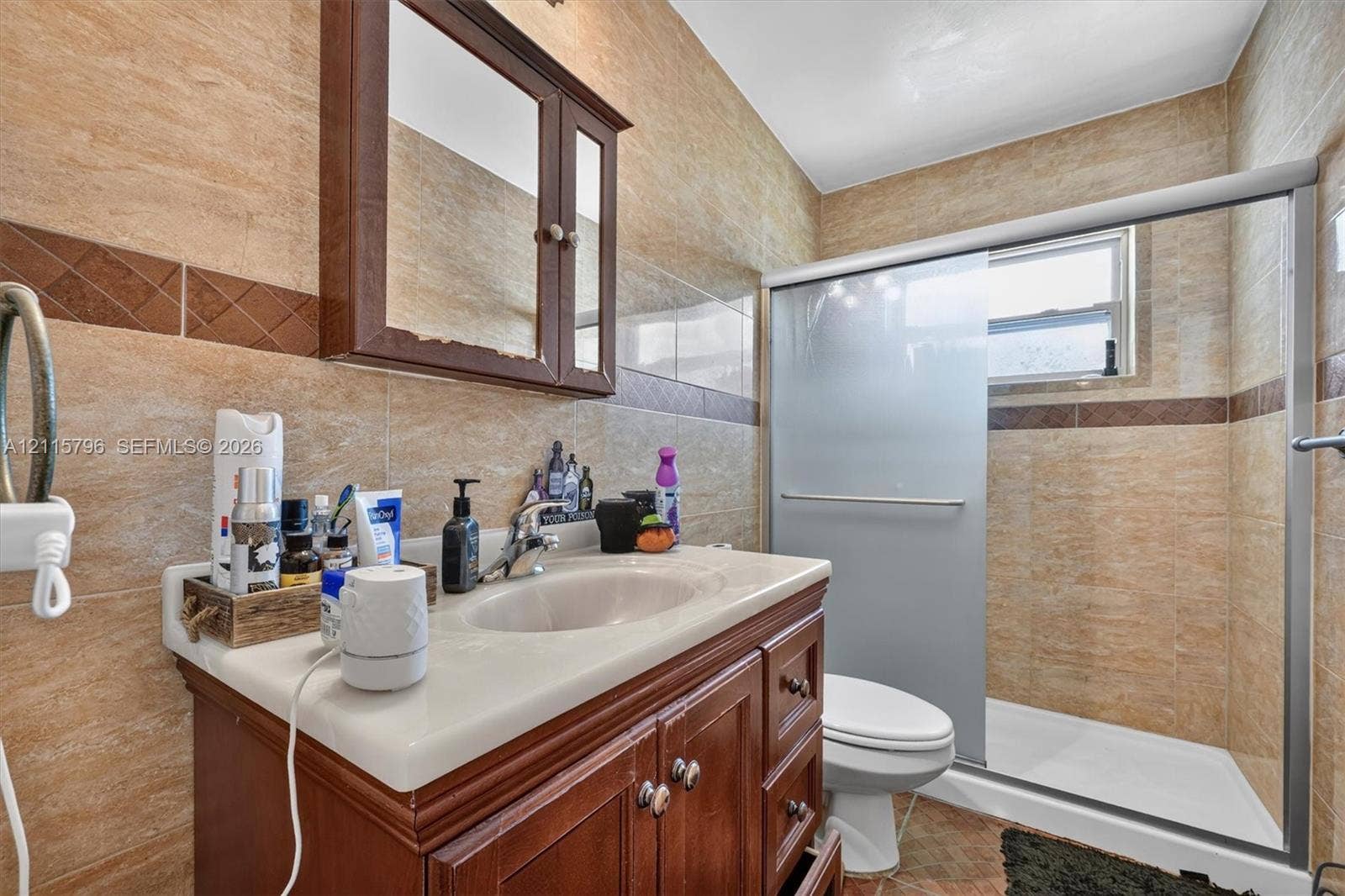 Bathroom featuring stone-finish wall tile with decorative mosaic inlay, wood-toned vanity cabinet, integrated countertop sink with chrome faucet, wall-mounted medicine cabinet, and glass-enclosed shower stall