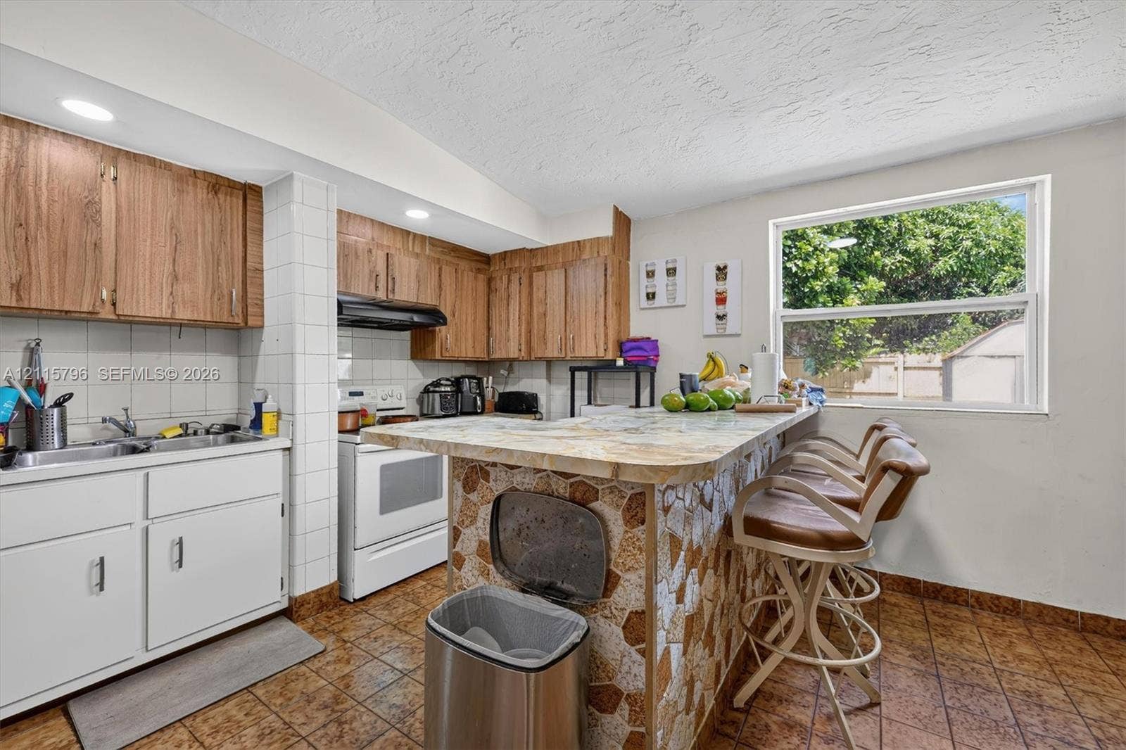 Kitchen featuring wood-finish upper cabinetry, white lower cabinetry, tile-topped peninsula with stone-finish base, and recessed lighting