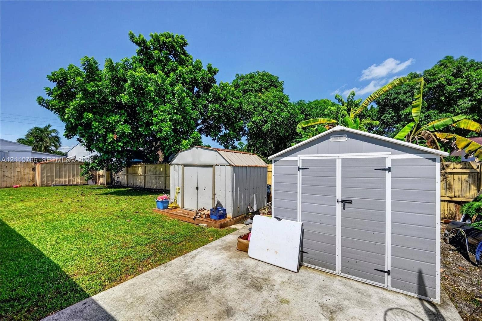 Backyard featuring a concrete patio, two exterior storage sheds, and perimeter wood fencing