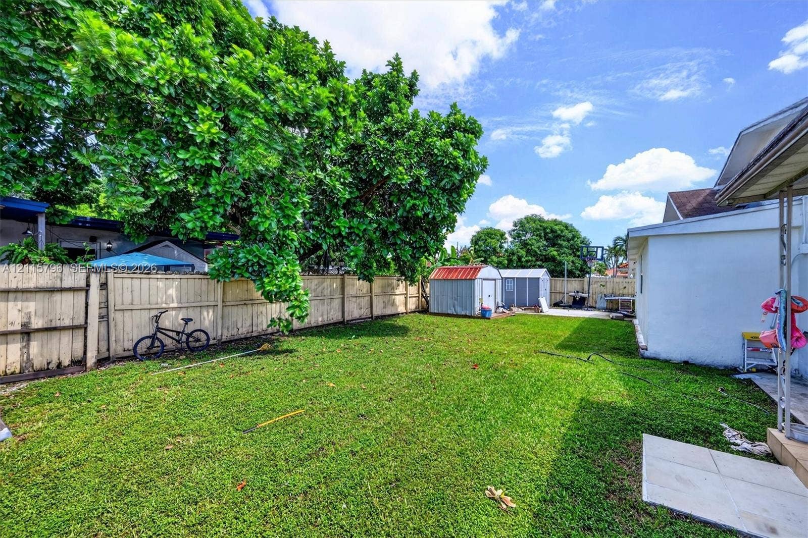 Expansive backyard featuring a manicured lawn, perimeter wood fencing, and two detached metal storage structures