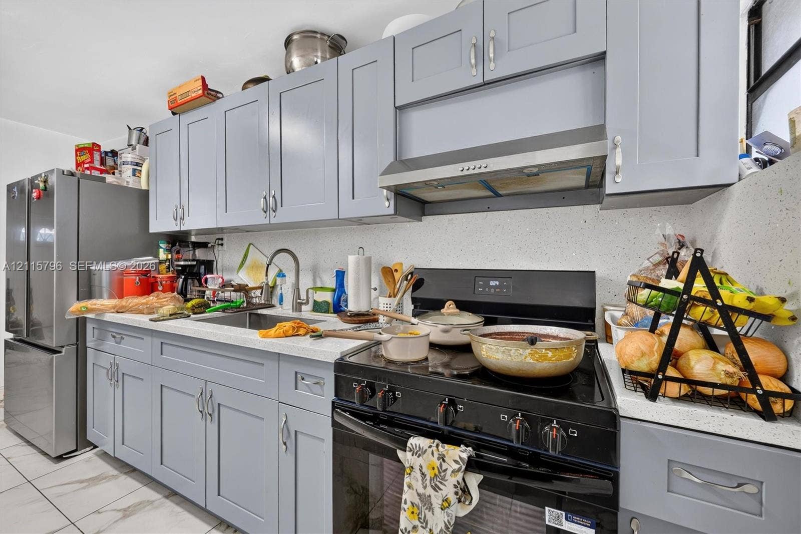 Kitchen featuring shaker-style cabinetry, quartz countertops, stainless steel undermount sink, integrated range hood, and tile flooring