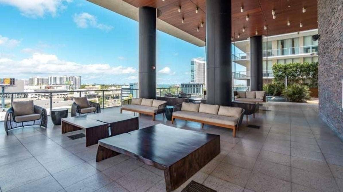 Expansive covered terrace featuring large-format stone tile flooring, structural columns, wood-paneled ceiling with recessed lighting, and a stone-clad feature wall