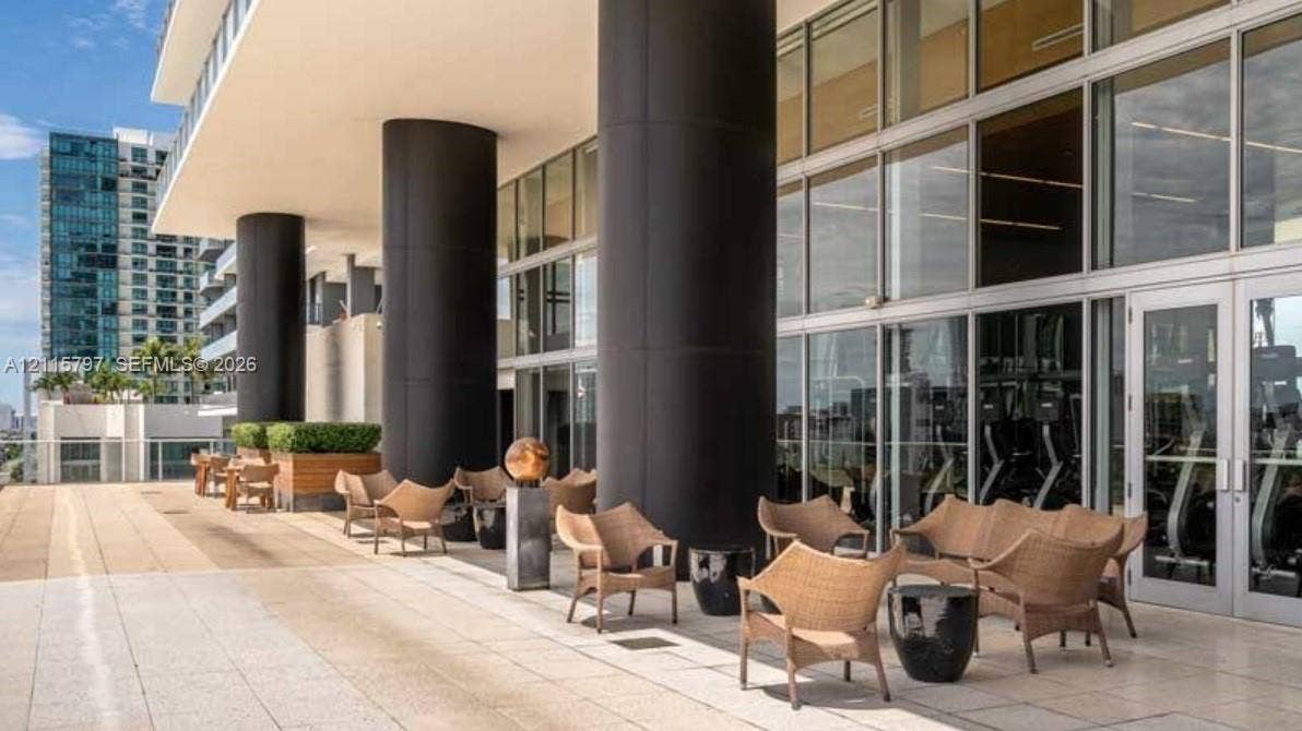 Expansive outdoor terrace featuring stone tile flooring, prominent structural columns, and floor-to-ceiling glass wall panels