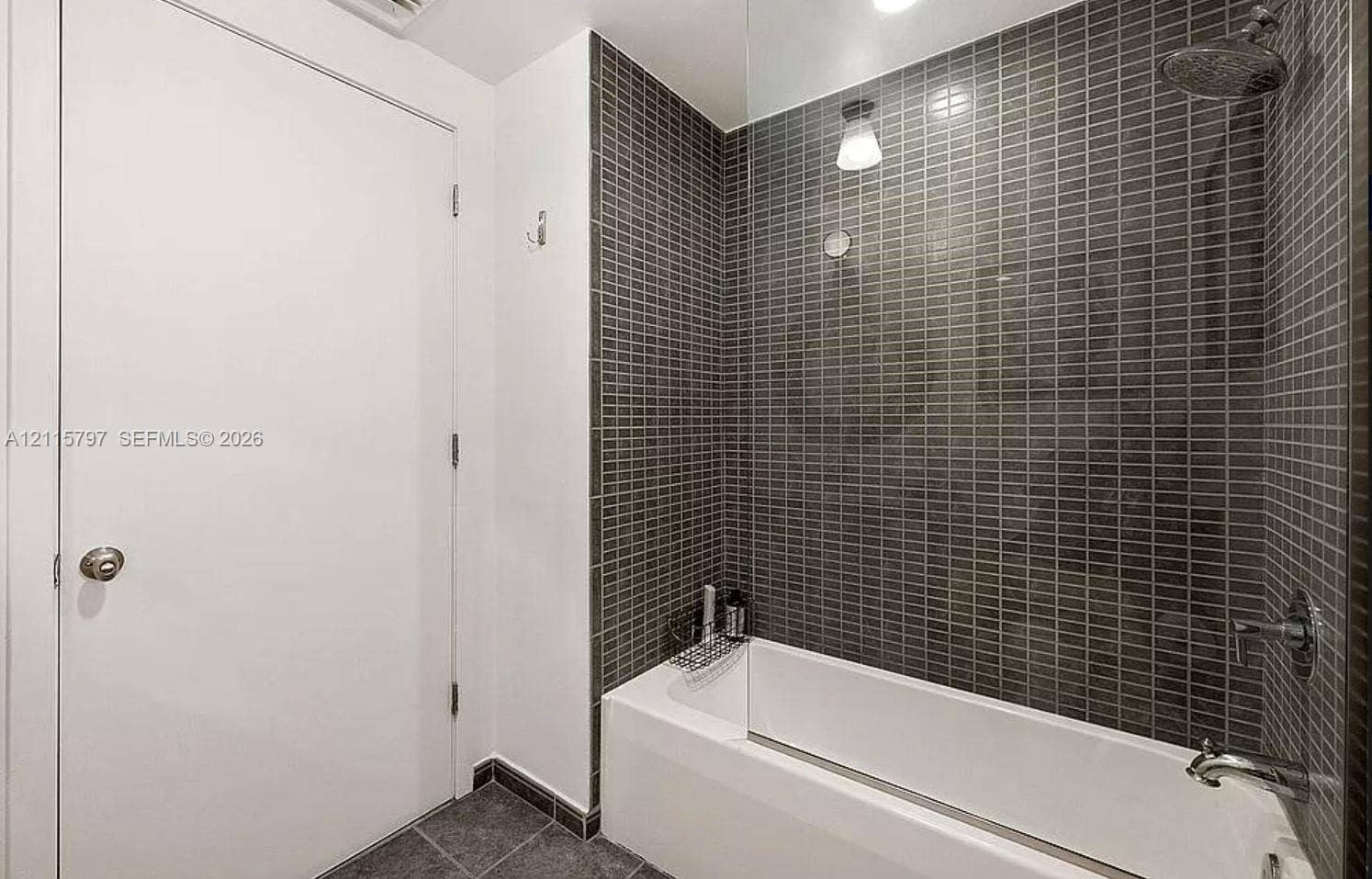 Bathtub featuring a glass shower panel, charcoal-toned mosaic tile surround, and polished chrome rainfall showerhead