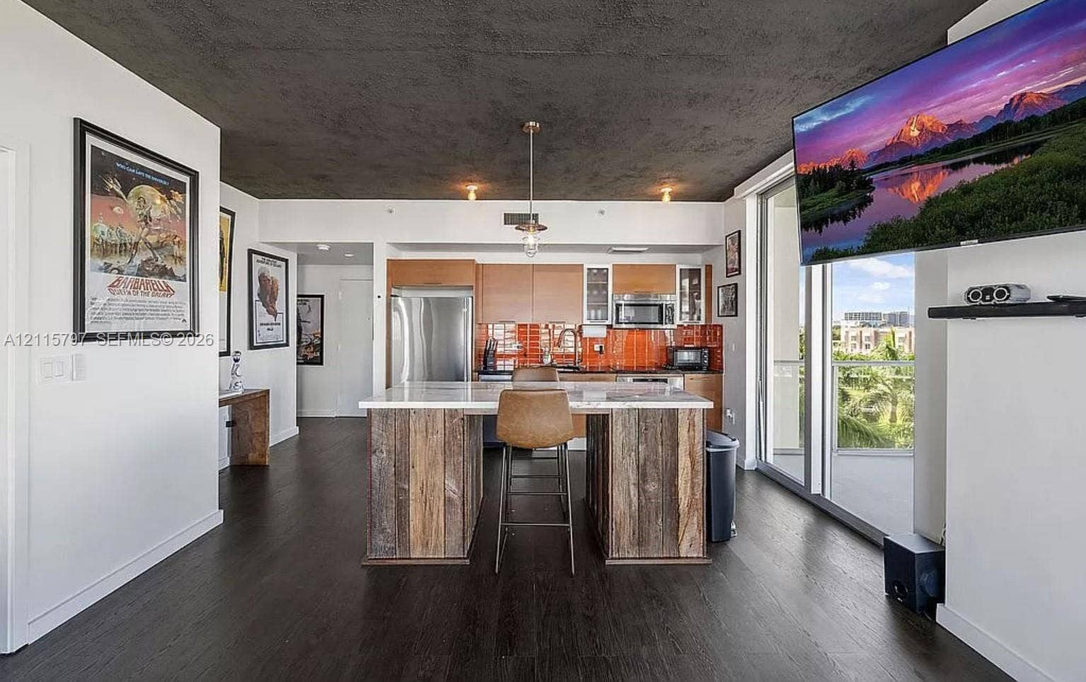 Open kitchen featuring wood-finish flooring, a central island with natural wood cabinetry and a stone countertop, orange glass tile backsplash, and stainless steel appliances