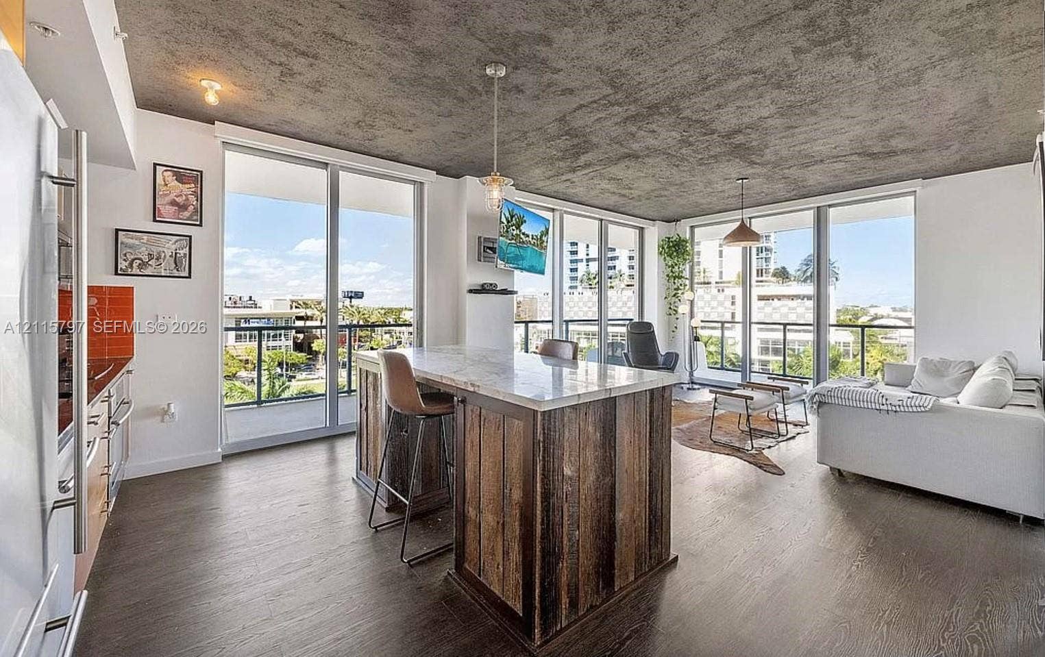 Open-concept living space featuring a textured concrete ceiling, wood-finish flooring, floor-to-ceiling glass doors, and a central island with a stone countertop and reclaimed wood paneling